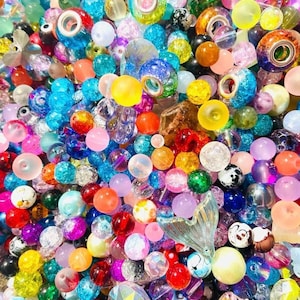 May include: A vibrant assortment of colorful beads in various shapes and sizes. The beads are a mix of transparent, opaque, and patterned designs, including round, faceted, and decorative styles. Colors include blue, pink, yellow, orange, and green.