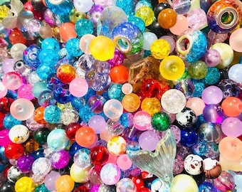 Puede incluir: Un vibrante surtido de cuentas de colores en varias formas y tamaños. Las cuentas son una mezcla de diseños transparentes, opacos y estampados, incluyendo estilos redondos, facetados y decorativos. Los colores incluyen azul, rosa, amarillo, naranja y verde.