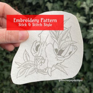 May include: A white embroidery pattern featuring a detailed line drawing of an animal skull with leaves. The text "Embroidery Pattern Stick & Stitch Style" is at the top of the pattern. The text "@horrorpopdesigns" is at the bottom of the pattern.