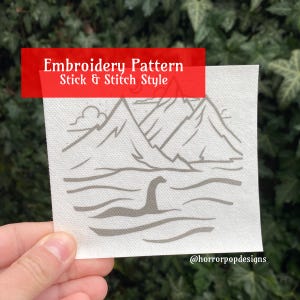 May include: Embroidery pattern for a stick and stitch style design of a mythical sea monster in a lake with mountains in the background. The pattern is printed on white fabric.