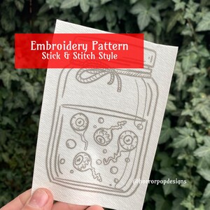 May include: Embroidery pattern for a jar filled with eyeballs. The pattern is in a stick and stitch style. The text "Embroidery Pattern Stick & Stitch Style" is at the top of the image. The text "@horrorpopdesigns" is at the bottom of the image.