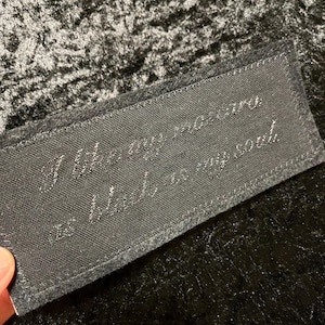 May include: A rectangular black fabric patch with the embroidered text "I like my mascara as black as my soul." The patch is made of a textured material and is set against a dark, velvety background.