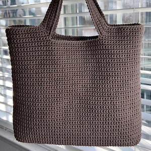 May include: A brown crocheted tote bag with two handles. The bag is made with a simple stitch pattern.