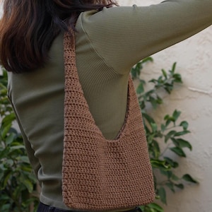 May include: A brown crocheted shoulder bag with a wide strap. The bag is worn over a green long-sleeved shirt.