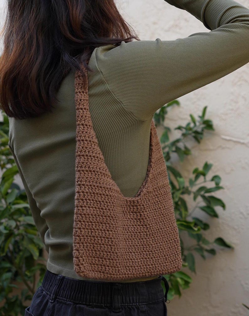 May include: A brown crocheted shoulder bag with a wide strap. The bag is worn over a green long-sleeved shirt.