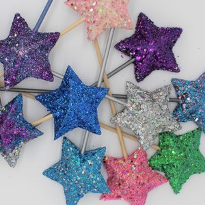 May include: Assortment of glitter star wands in various colors, including pink, purple, blue, silver, green, and light blue. The wands are made of wood and have a star-shaped topper.