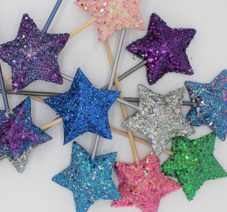 May include: Assortment of glitter star wands in various colors, including pink, purple, blue, silver, green, and light blue. The wands are made of wood and have a star-shaped topper.