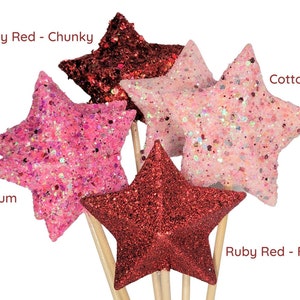 May include: Five glitter star-shaped ornaments on wooden sticks. The stars are in four colors: ruby red (chunky and fine), bubblegum pink, and cotton candy pink.