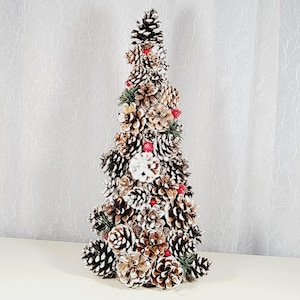May include: A small, snowy pine tree made of pine cones and decorated with red berries. The tree is a festive holiday decoration.