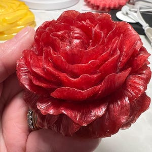 May include: A single red rose-shaped candle with a shiny, metallic finish. The candle is made to look like a real rose with multiple layers of petals.