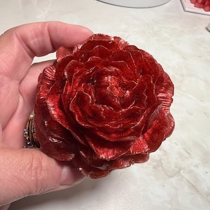 May include: A large, red, resin flower with a glossy finish. The flower has multiple layers of petals and resembles a peony.