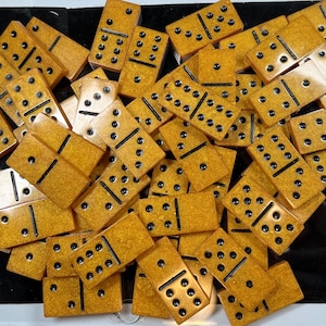 Könnte beinhalten: Ein Stapel gelber Dominosteine mit schwarzen Punkten. Die Dominosteine sind in einem zufälligen Muster angeordnet.
