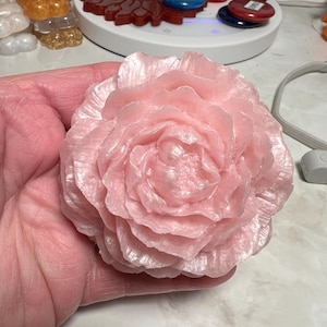 Puede incluir: Un gran jabón rosa hecho a mano con forma de rosa. El jabón tiene un acabado brillante y nacarado.