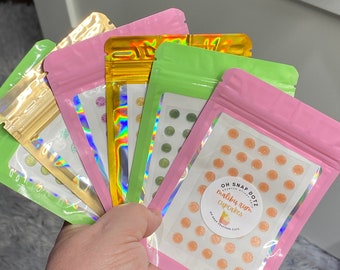 May include: Four resealable bags with different colored backgrounds, each containing small round sprinkles. The pink bag has a sticker that says "OH SNAP DOTZ" and "maliby rum cupcakes".