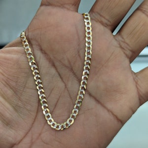May include: A gold-colored curb chain necklace with alternating gold and silver links. The chain is held in a hand, showcasing its design and texture. The necklace is a jewelry item.