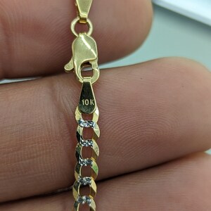 May include: Close-up of a gold chain with a lobster clasp. The chain links alternate between gold and silver-colored metal. The clasp is stamped with "10K". The chain is a jewelry item.