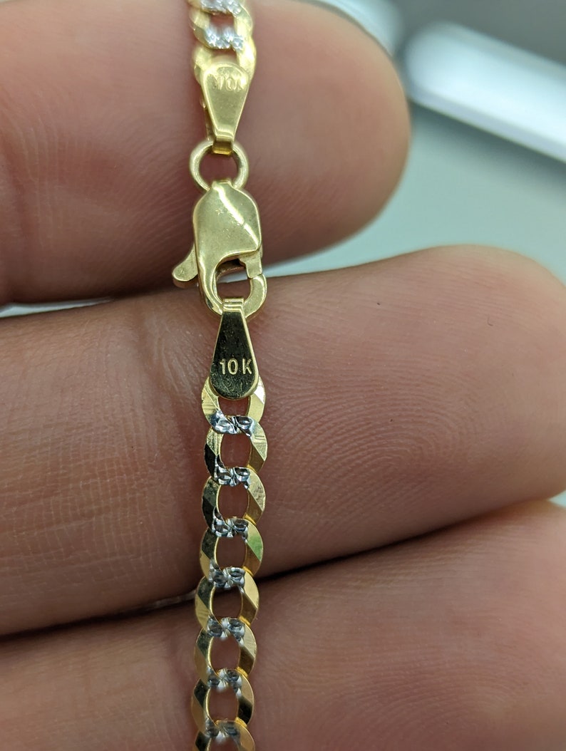 May include: Close-up of a gold chain with a lobster clasp. The chain links alternate between gold and silver-colored metal. The clasp is stamped with "10K". The chain is a jewelry item.