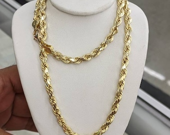 May include: A gold rope chain necklace on a white display stand. The chain is made of thick, twisted links.
