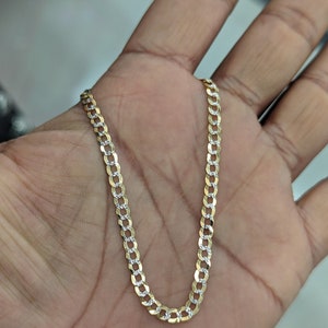 May include: A gold-colored curb chain necklace with alternating textured and smooth links. The chain is displayed on a hand, showcasing its design and texture. The necklace is a jewelry item.