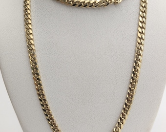 May include: A gold curb chain necklace with a lobster clasp. The chain is on a white display stand.