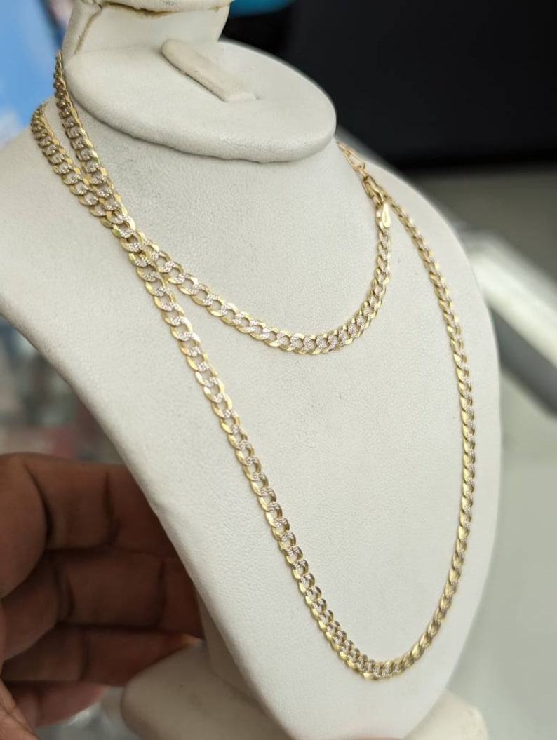 Pode incluir: Um colar de corrente de ouro com um design de corte de diamante. A corrente est&aacute; em um expositor branco.