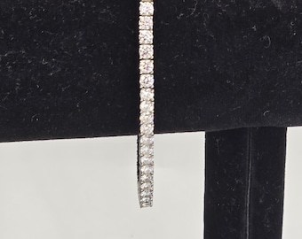 May include: A silver bracelet with a line of clear, square-cut stones. The bracelet is displayed against a black velvet background, showcasing its sparkle. The clasp is visible at the top.