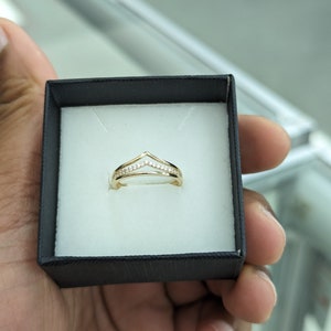 May include: A gold ring with a V-shaped design set with small clear stones.