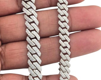 May include: Two silver-colored, diamond-studded bracelets with a Cuban link design. The bracelets are displayed side-by-side, showcasing their intricate weave and sparkling stones. The jewelry is held against a neutral background.
