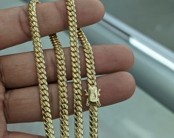 May include: A gold chain necklace with a curb link style. The chain is folded in half and held in a hand.