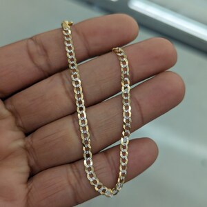 May include: A gold and silver curb chain necklace. The chain is made of alternating gold and silver links, creating a two-tone effect. The necklace is displayed against a neutral background.