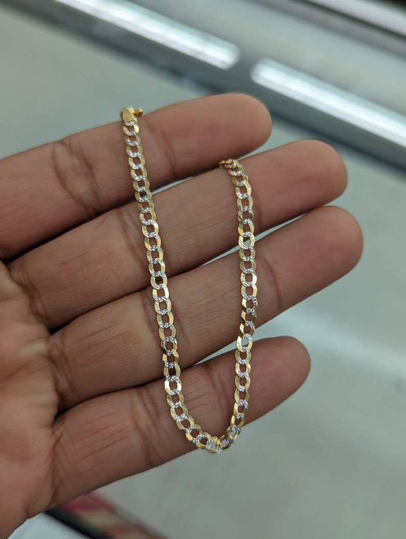 May include: A gold and silver curb chain necklace. The chain is made of alternating gold and silver links, creating a two-tone effect. The necklace is displayed against a neutral background.