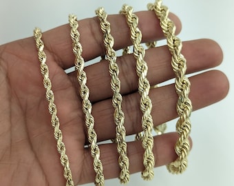 May include: A set of six gold rope chains of varying lengths and thicknesses. The chains are arranged in a hand, with the thickest chain at the top and the thinnest chain at the bottom.