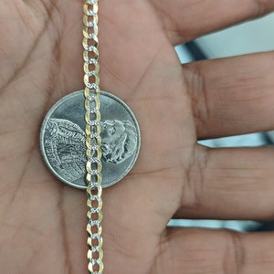 May include: A gold and silver curb chain necklace is displayed next to a coin. The chain has alternating gold and silver links. The necklace is approximately 0.1 inches wide.