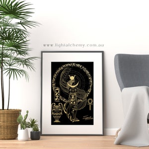 Könnte beinhalten: Gerahmter Kunstdruck mit einer goldenen Illustration einer ägyptischen Gottheit auf schwarzem Hintergrund. Das Kunstwerk enthält Hieroglyphen, eine geflügelte Figur mit einem Halbmond-Kopfschmuck und den Text "www.lighialchemy.com.au". Der Druck wird auf einer Holzoberfläche präsentiert.