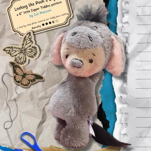 Può includere: Un orsacchiotto di peluche grigio Eeyore con un naso rosa e una lunga coda. L'orso è seduto su uno sfondo di carta marrone con uno sfondo di carta blu e bianco dietro. L'immagine include anche un ago da cucire, delle forbici e due occhietti tondi. L'immagine include il testo "Looking like Pooh's Eeyore a 6" little Dipper Teddies pattern by Cat Maessen" e "a step by step photo tutorial for teddy bear making, difficulty: ☆☆☆".