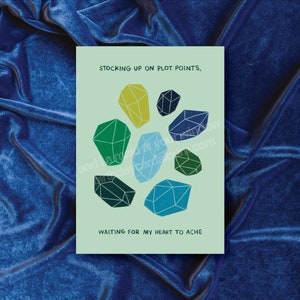 May include: A light green card with the text "STOCKING UP ON PLOT POINTS, WAITING FOR MY HEART TO ACHE" and a design of seven colorful geometric shapes resembling gemstones.