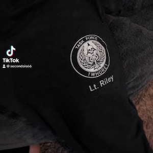 May include: Black sweatpants with a white circular emblem featuring a skull, wings, and the words "TASK FORCE" and "1 WHORE". The text "Lt. Riley" is below the emblem. The TikTok logo and username are visible in the upper left corner.