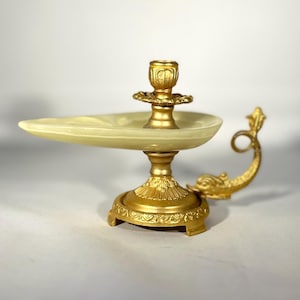 Peut inclure: Un bougeoir en métal doré avec un plat en céramique blanche. Le bougeoir est décoré d'un motif et d'une poignée incurvée.