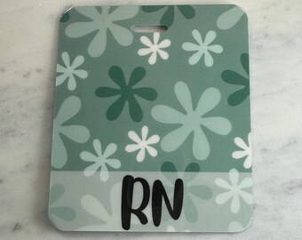 May include: A rectangular badge with a floral pattern in shades of green and white. The badge has the letters "RN" in black. The word "Front" is printed at the top. The badge is on a white marble surface.