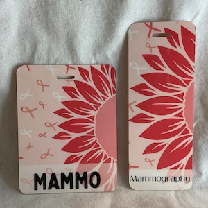 Puede incluir: Dos porta-credenciales rectangulares con esquinas redondeadas. Uno presenta un dise&ntilde;o de girasol rosa y la palabra "MAMMO" en negro. El otro tiene un dise&ntilde;o similar con la palabra "Mammography". Ambos tienen acentos de cinta rosa.
