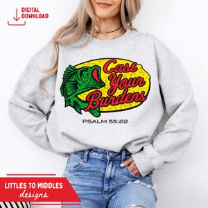 Op de afbeelding: Een lichtgrijze sweatshirt met een groene visafbeelding en de woorden "Cast Your Burdens" in geel en rood. De tekst "PSALM 55:22" staat onder de afbeelding. De woorden "DIGITAL DOWNLOAD" staan in de linkerbovenhoek.