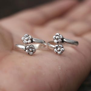 Puede incluir: Cuatro anillos de plata para el dedo del pie, cada uno con un pequeño y detallado diseño floral. Los anillos se muestran sobre una superficie clara, destacando los intrincados detalles florales y la calidad reflectante del metal. Los anillos son ajustables.