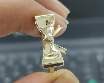 May include: A gold bow ring with a smooth, polished finish. The ring is designed in the shape of a bow with a knot in the center.