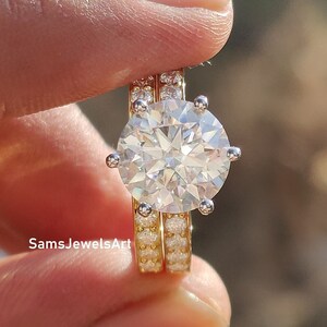 May include: A two-piece ring set featuring a large, round, clear, sparkling diamond-like stone surrounded by smaller stones. The ring is set in yellow gold with a white gold band.