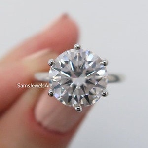 Puede incluir: Un anillo de plata con una piedra grande, redonda y transparente similar a un diamante engastada en un engaste de seis garras.