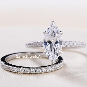 May include: A marquise cut diamond engagement ring set with a matching wedding band. Both rings feature a pave setting with small diamonds.