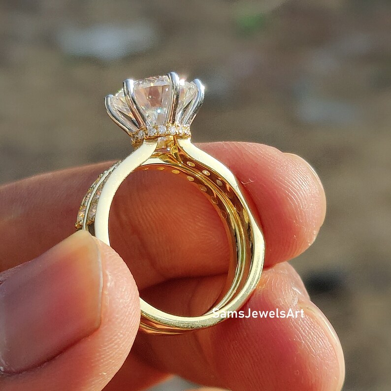 May include: A gold engagement ring set with a large, round, clear center stone surrounded by smaller stones. The ring is set on a band with a delicate, floral design.