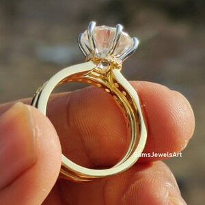May include: A gold ring set with a large, clear, round gemstone surrounded by smaller gemstones. The ring is set on a finger.