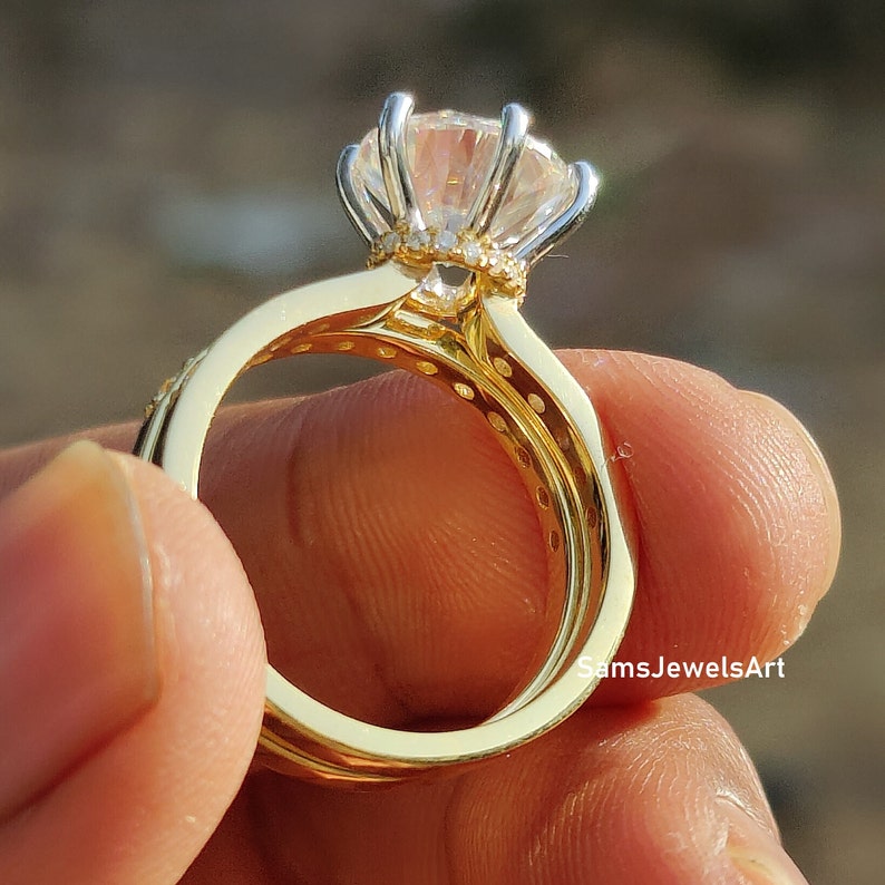 May include: A gold ring set with a large, clear, round gemstone surrounded by smaller gemstones. The ring is set on a finger.
