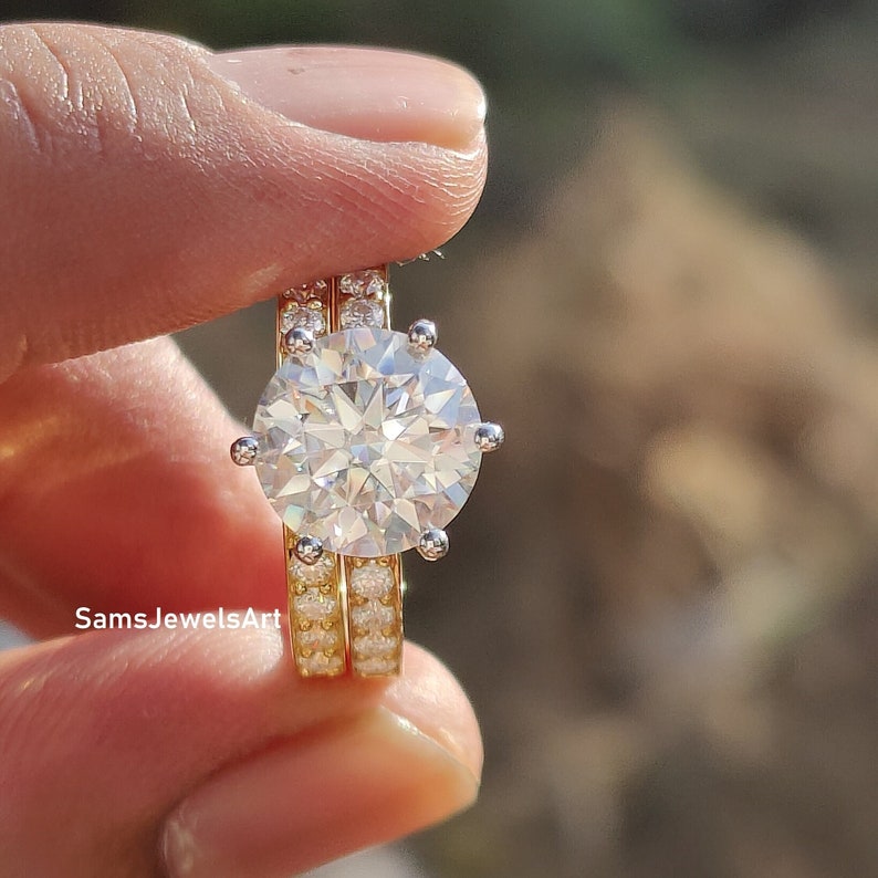 May include: A two-piece ring set featuring a large, round, clear, sparkling diamond-like stone surrounded by smaller stones. The ring is set in yellow gold with a white gold band.